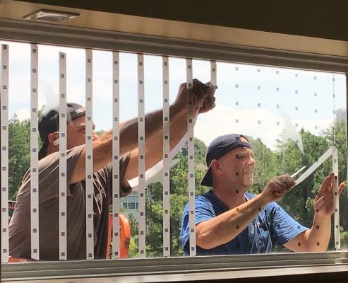 Workers install window film with visible dots to prevent birds from flying into Southface's windows.