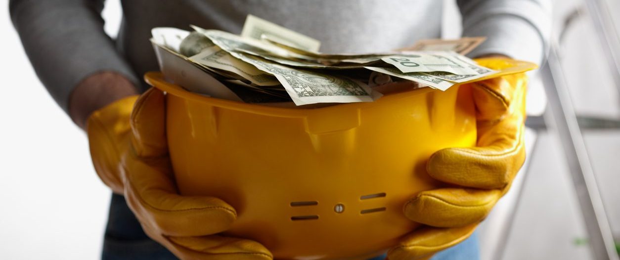 Construction worker holding yellow hard hat with dollars in it